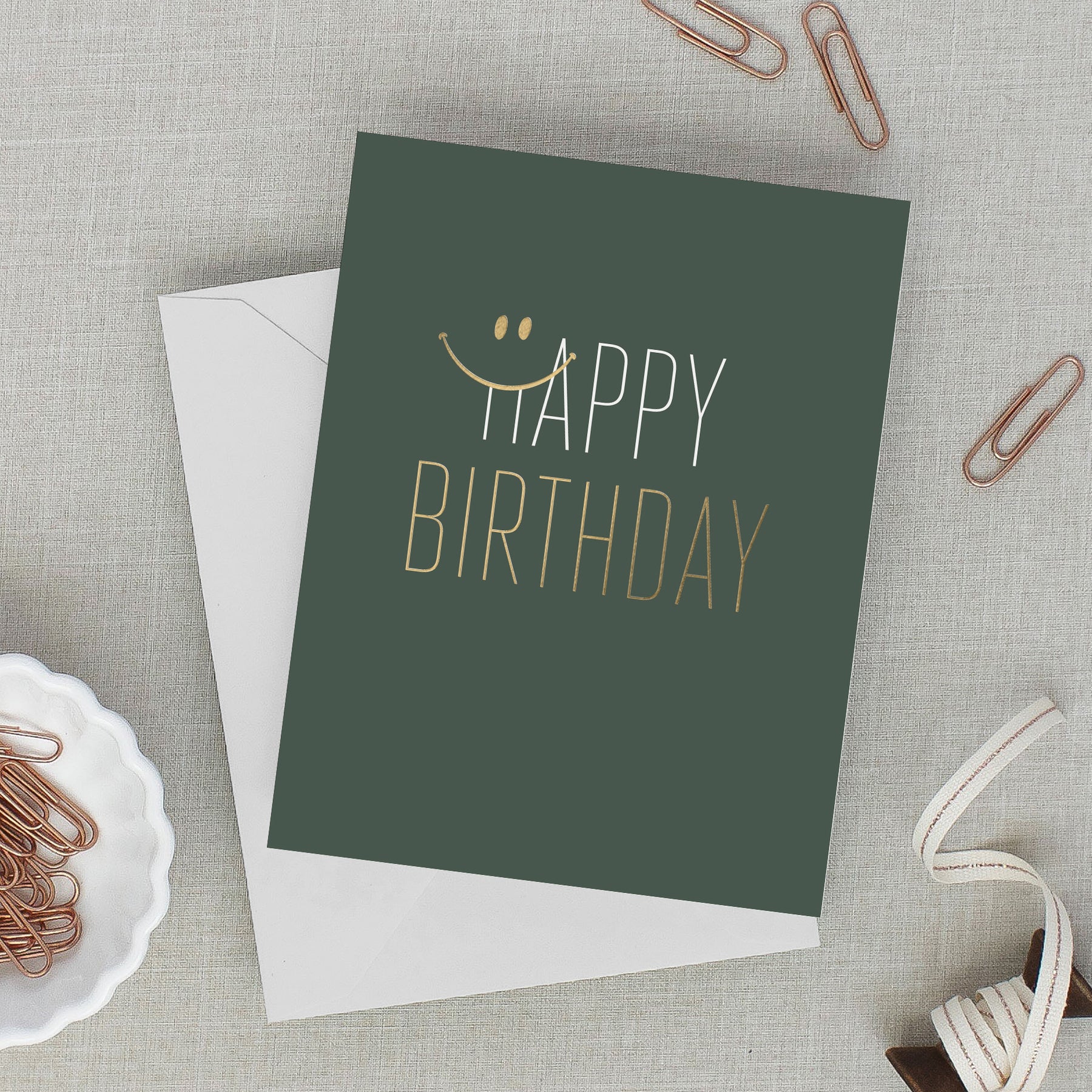 Green birthday card with 'Happy Birthday' text on a gray surface with paper clips.