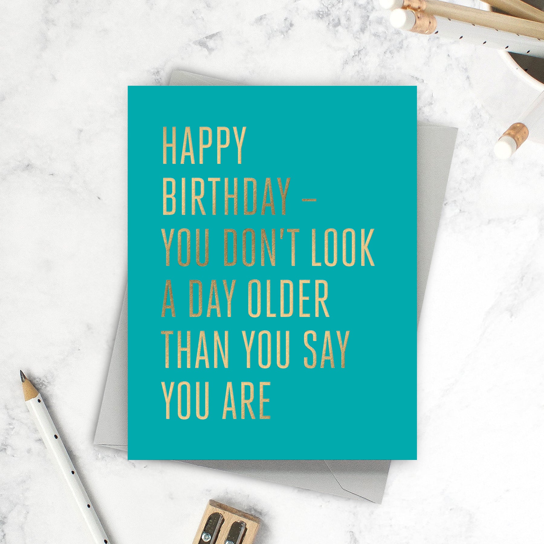 Turquoise birthday card with gold foil text on a marble surface