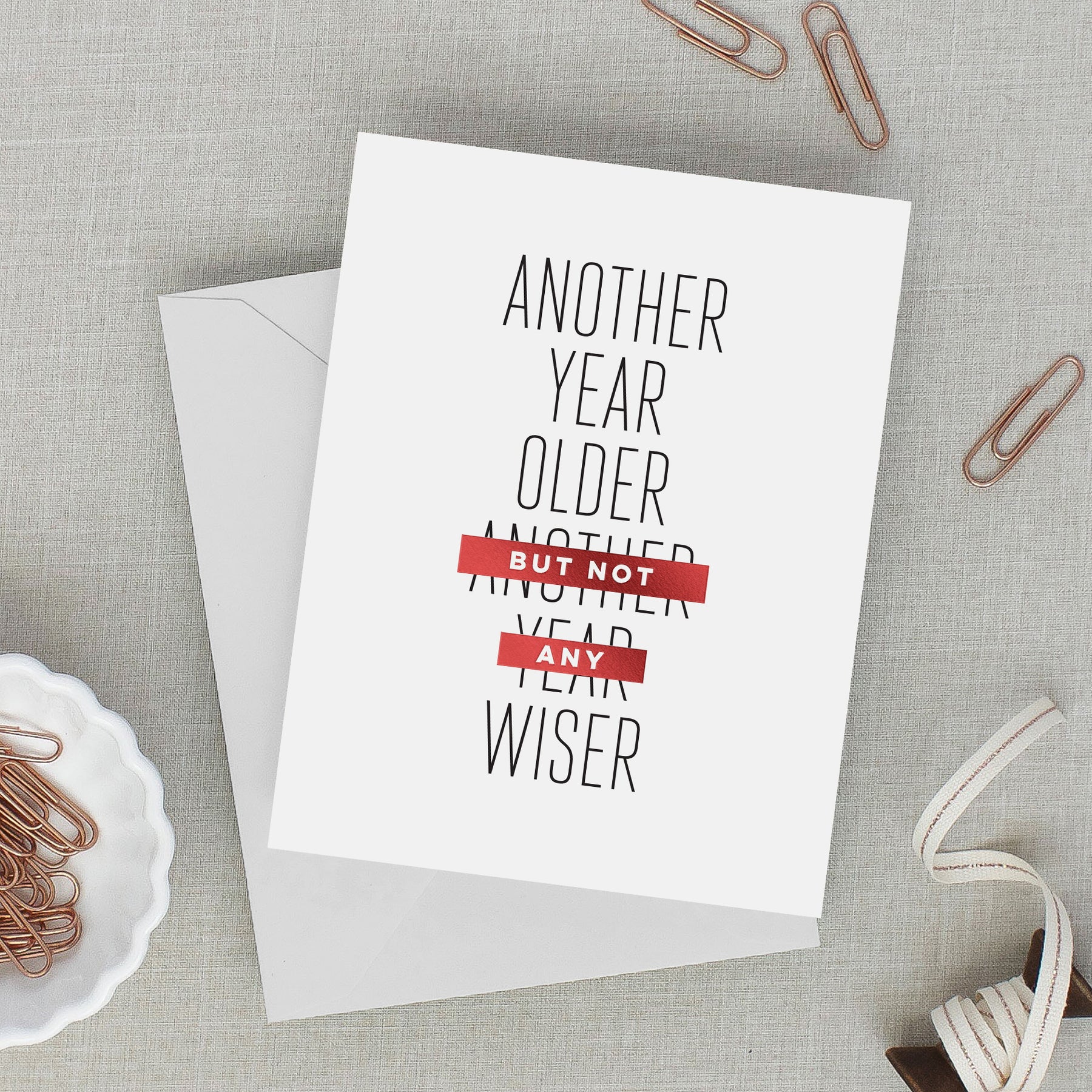 Greeting card with text 'Another year older, but not any year wiser' on a gray surface with paper clips.