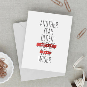 Greeting card with text 'Another year older, but not any year wiser' on a gray surface with paper clips.