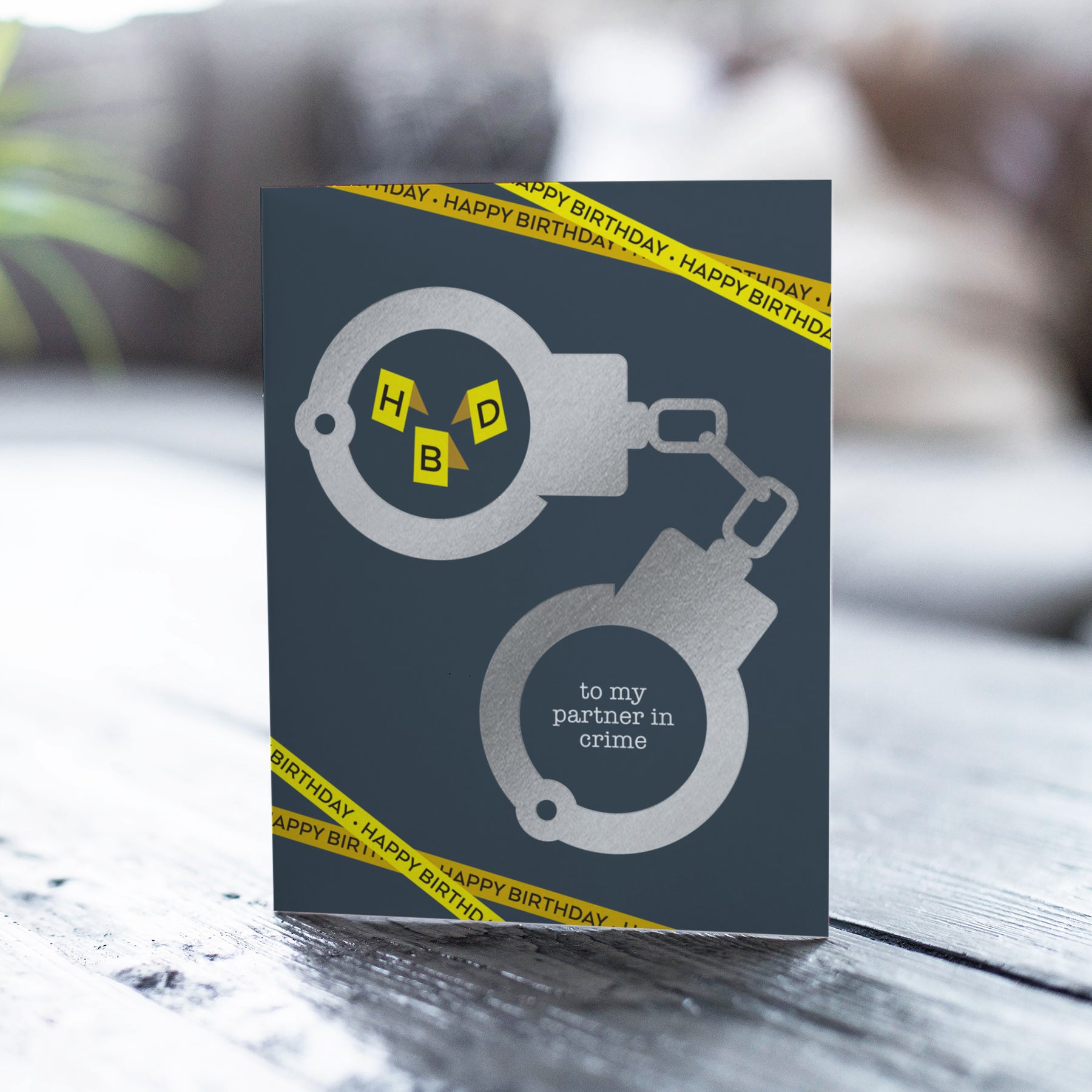 Greeting card with handcuffs design and 'to my partner in crime' text on a wooden surface.