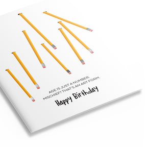 Three quarter view of birthday card with yellow pencils. Card reads "Age is just a number. Mischief? That's an art form."
