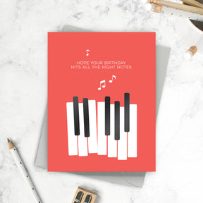 Greeting card with piano keys design and birthday message on a marble surface.