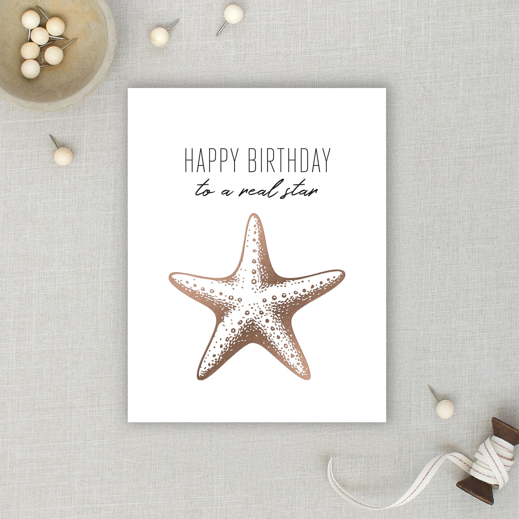 Card with a starfish illustration and 'Happy Birthday to a real star' text on a textured surface.