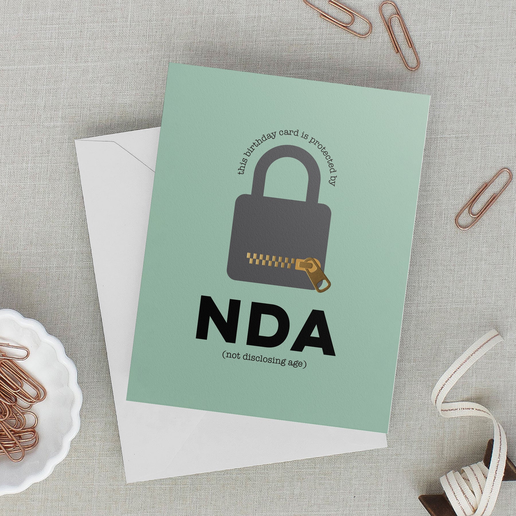 Lifestyle photo with green birthday card featuring a padlock with a message that reads "the birthday card is protected by NDA – not disclosing age"