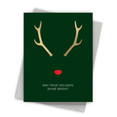 Greeting card with gold antlers and red nose on a green background, featuring the text 'May your holidays shine bright'.