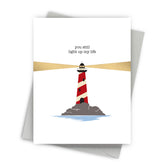 Greeting card with a lighthouse illustration and text 'you still light up my life' on a white background.