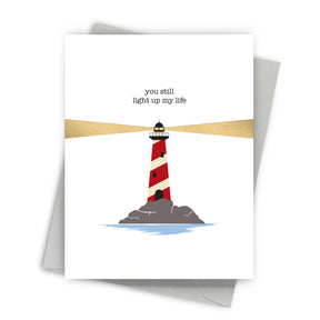 Greeting card with a lighthouse illustration and text 'you still light up my life' on a white background.