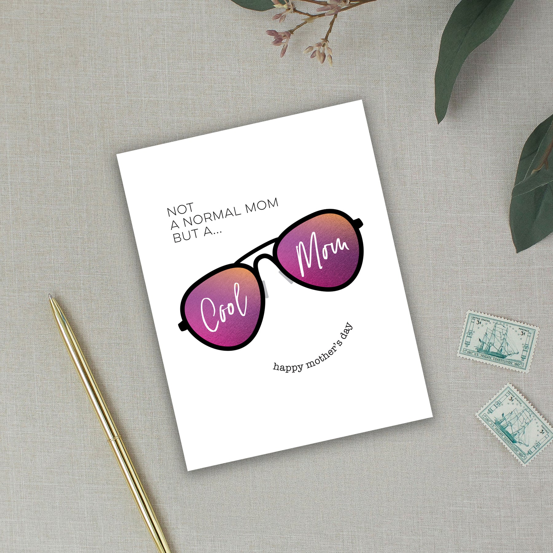 Greeting card with sunglasses illustration and text on a textured surface with a pen and stamps.