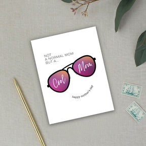 Greeting card with sunglasses illustration and text on a textured surface with a pen and stamps.