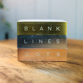 Stack of three notepads with 'Blank, Lines, and Dots' text on a wooden surface