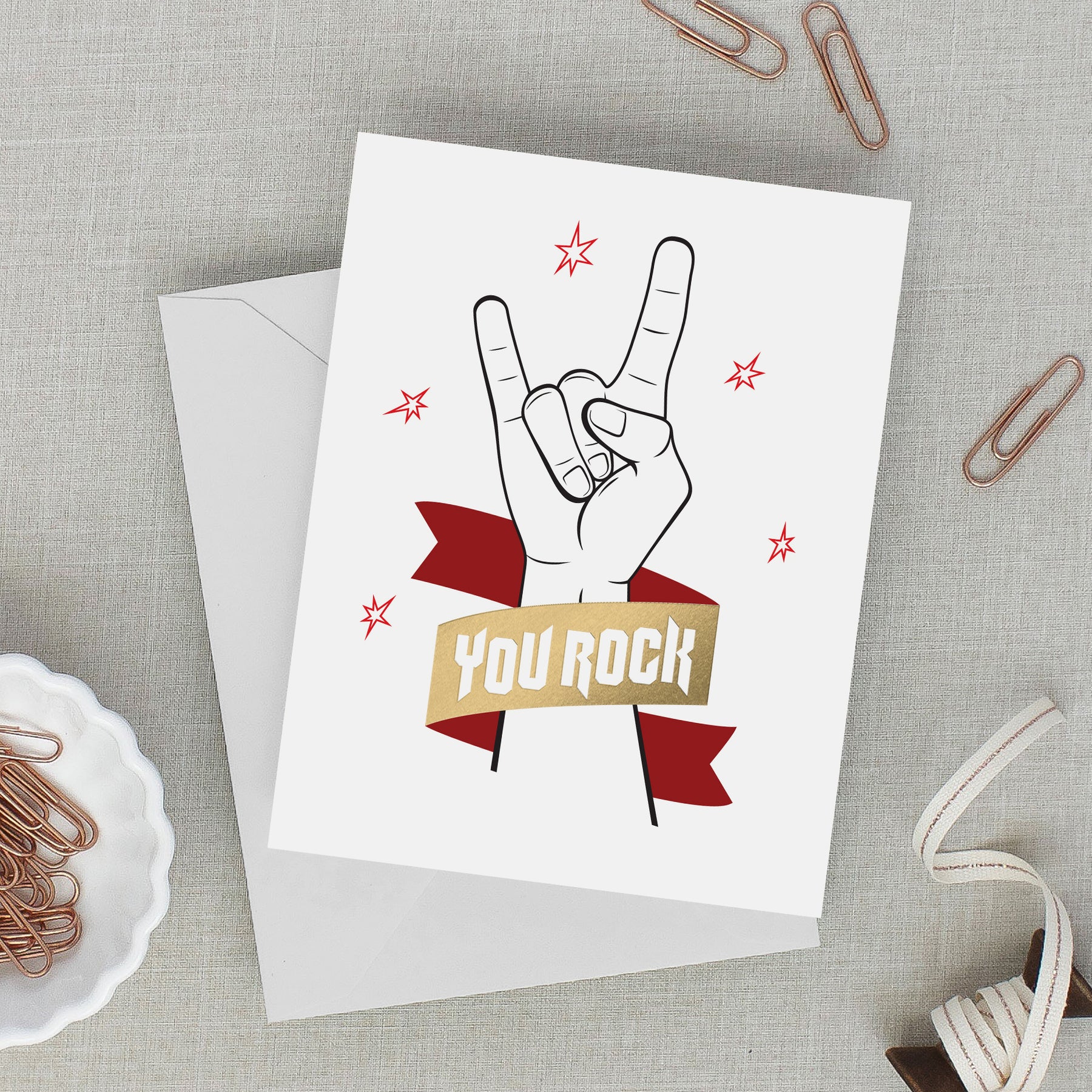 Greeting card with hand gesture and 'You Rock' text on a gray surface with paper clips.