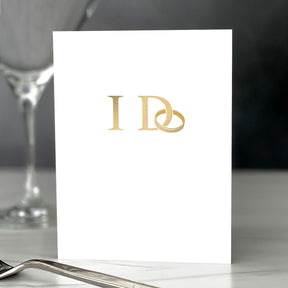 White card with gold monogram on a table setting with a glass and fork.